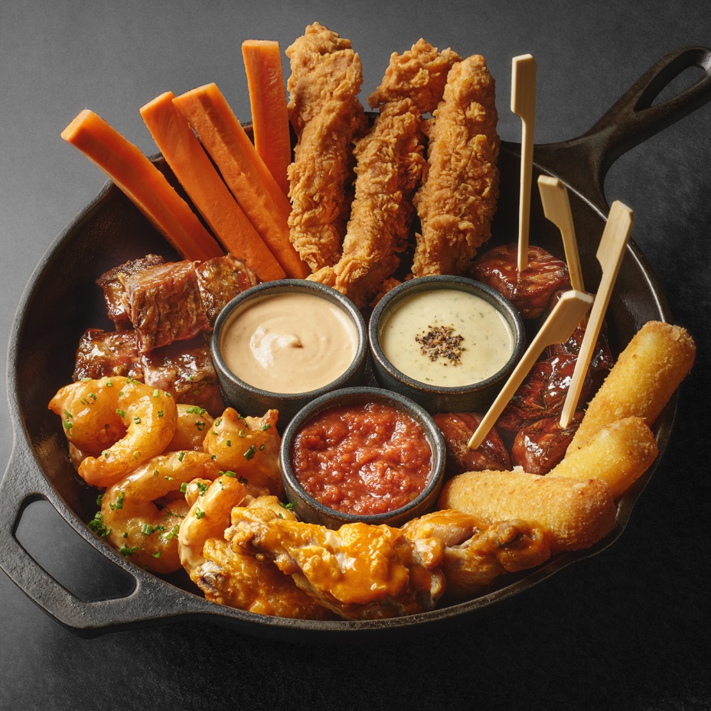 A cast iron skillet filled with various appetizers including chicken wings, shrimp, steak bites, and fries.