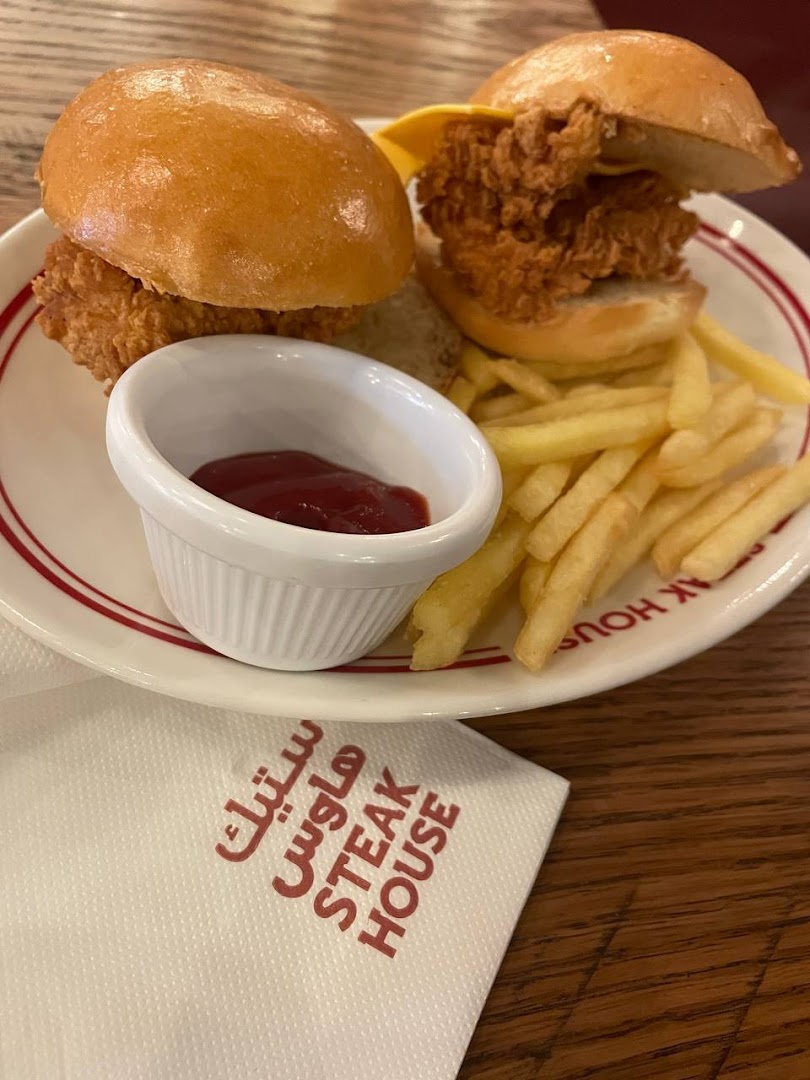 Two mini chicken burgers with fries and ketchup on a plate with a Steak House napkin.