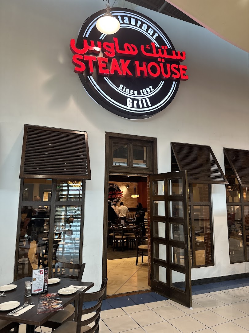 The entrance to a Steak House restaurant with a prominent sign and tables set for dining.