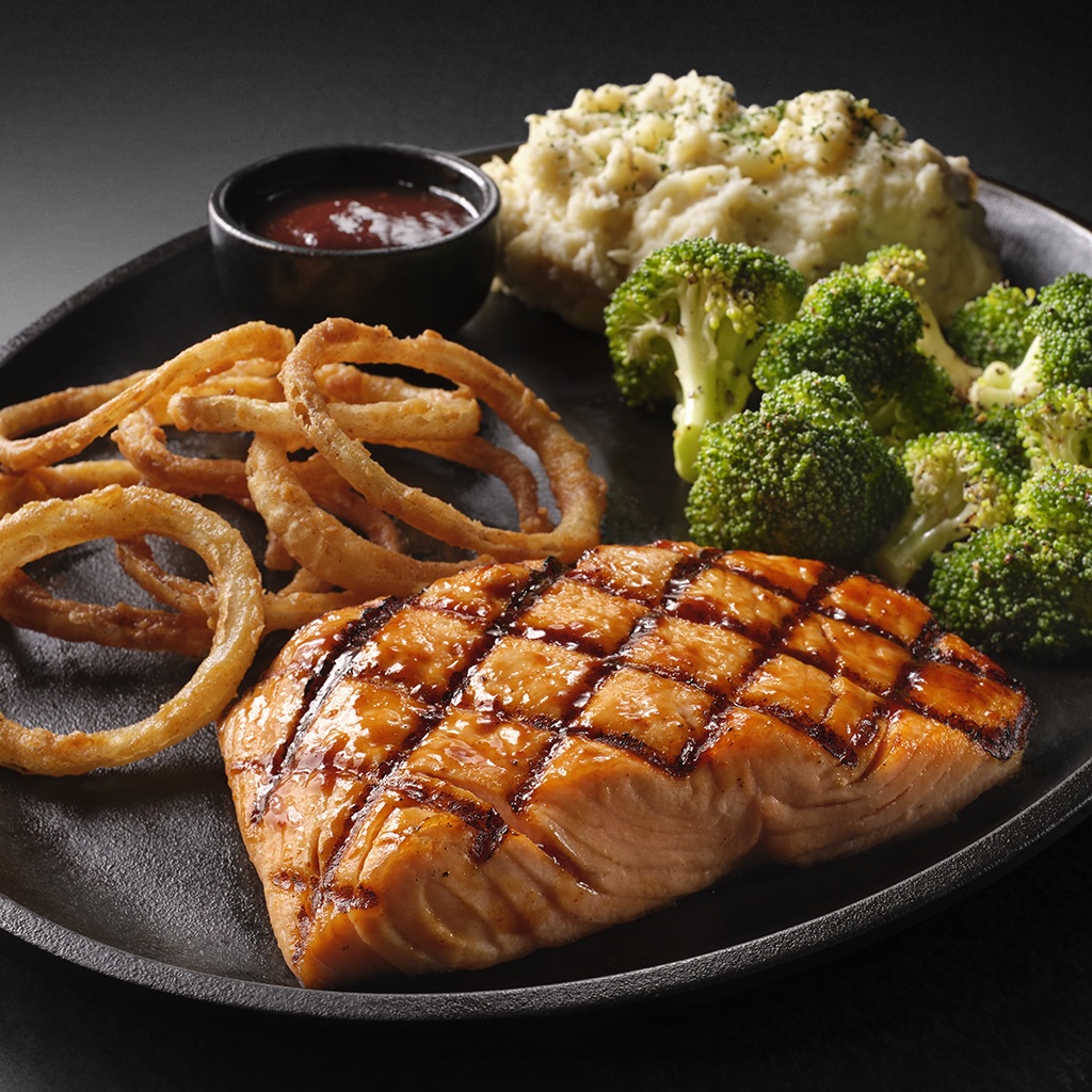 A grilled salmon fillet with mashed potatoes, broccoli, onion rings, and dipping sauce.
