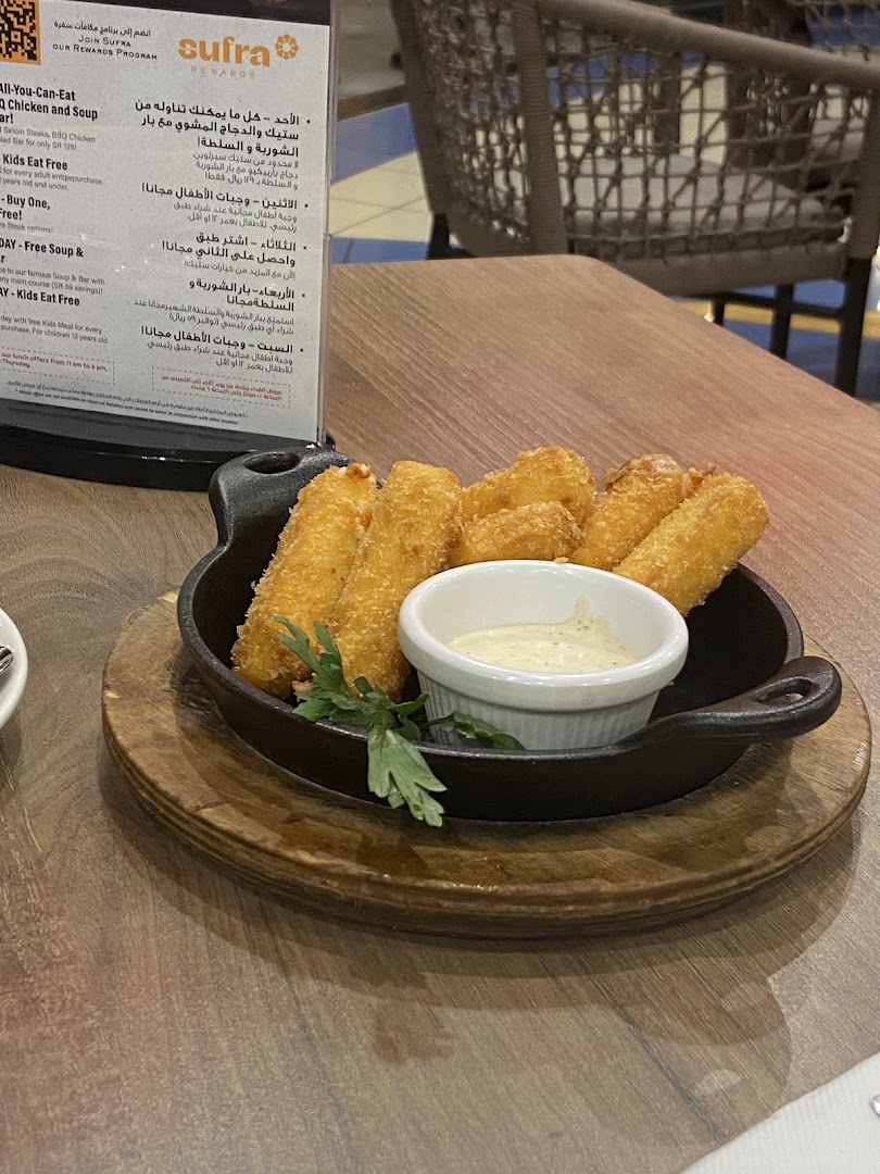 A plate of fried mozzarella sticks with dipping sauce on a wooden table.