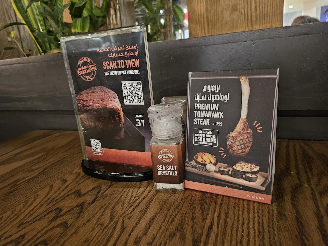 A table at a steakhouse with a menu, a salt shaker, and a promotional card for a Tomahawk steak.