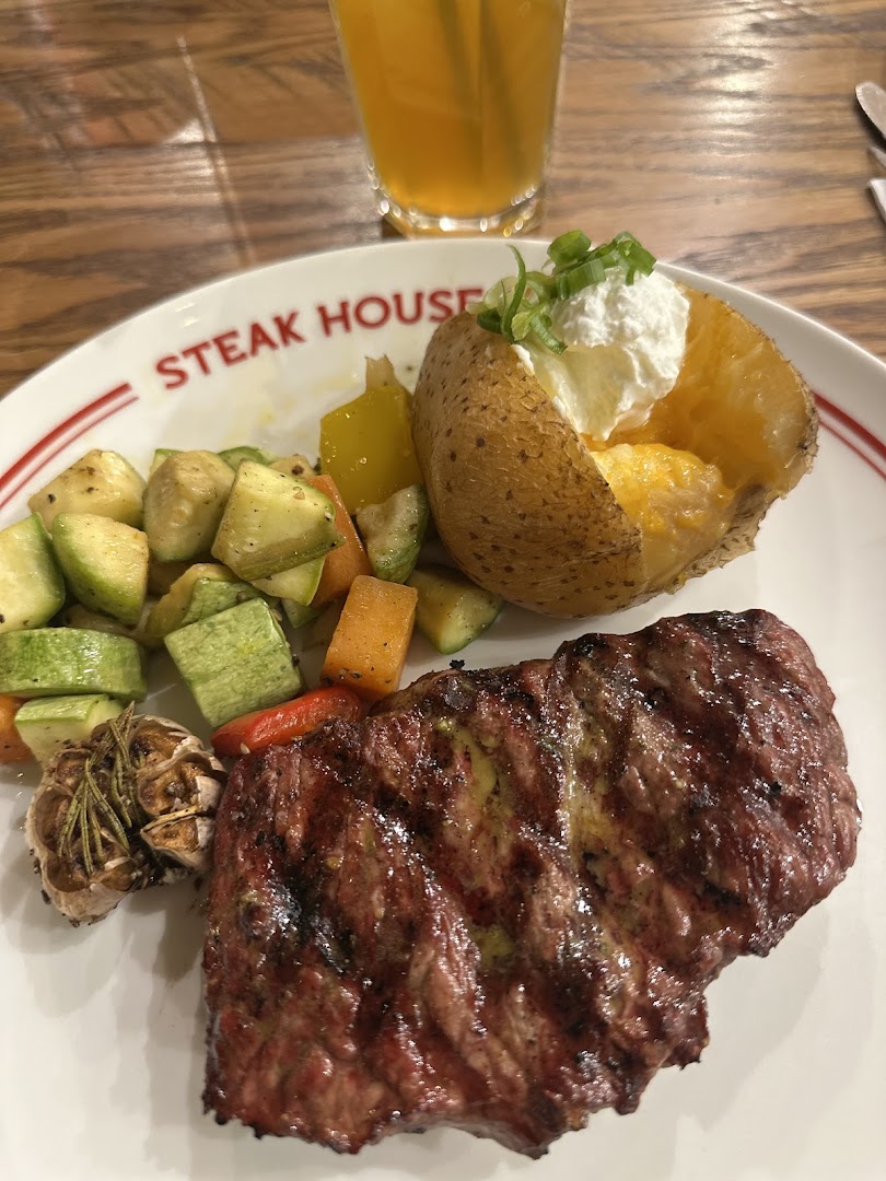A juicy steak with a baked potato and grilled vegetables, served with a drink.