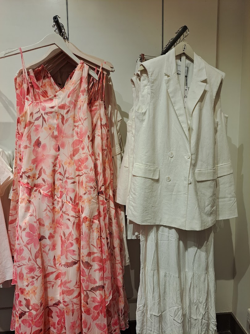 A floral print dress and a white linen vest with a tiered skirt are displayed on hangers.