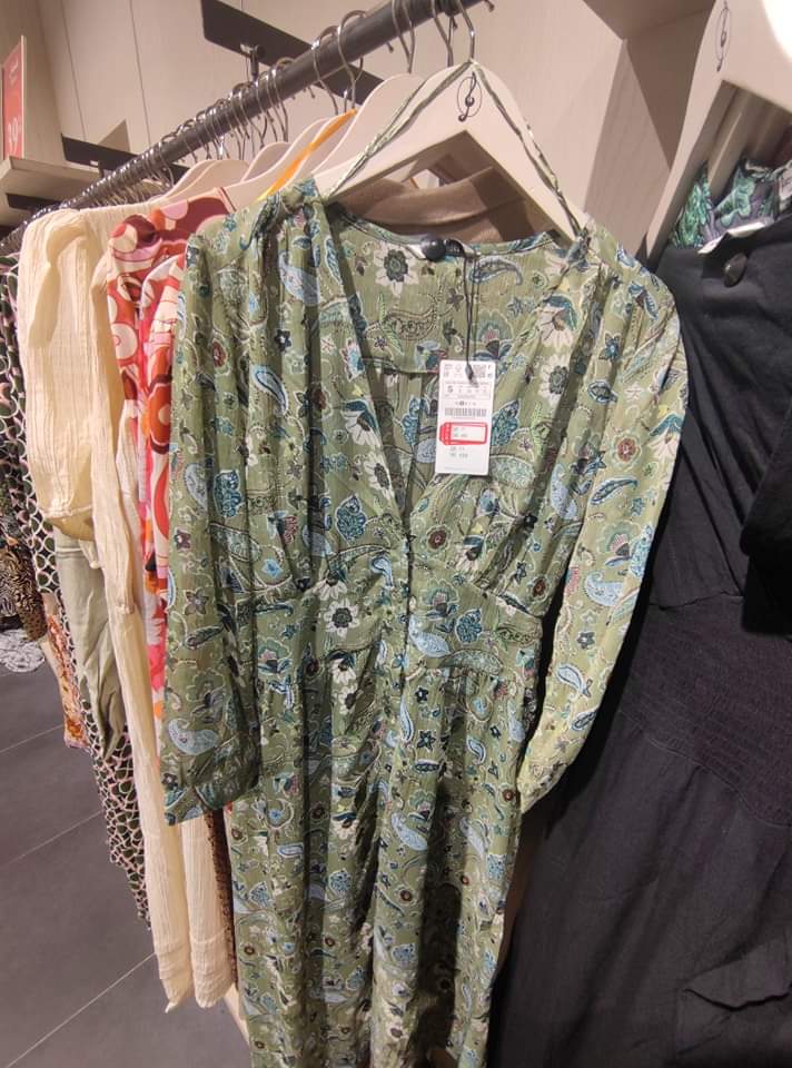 A green paisley print dress with a V-neck and button detailing hangs on a rack.