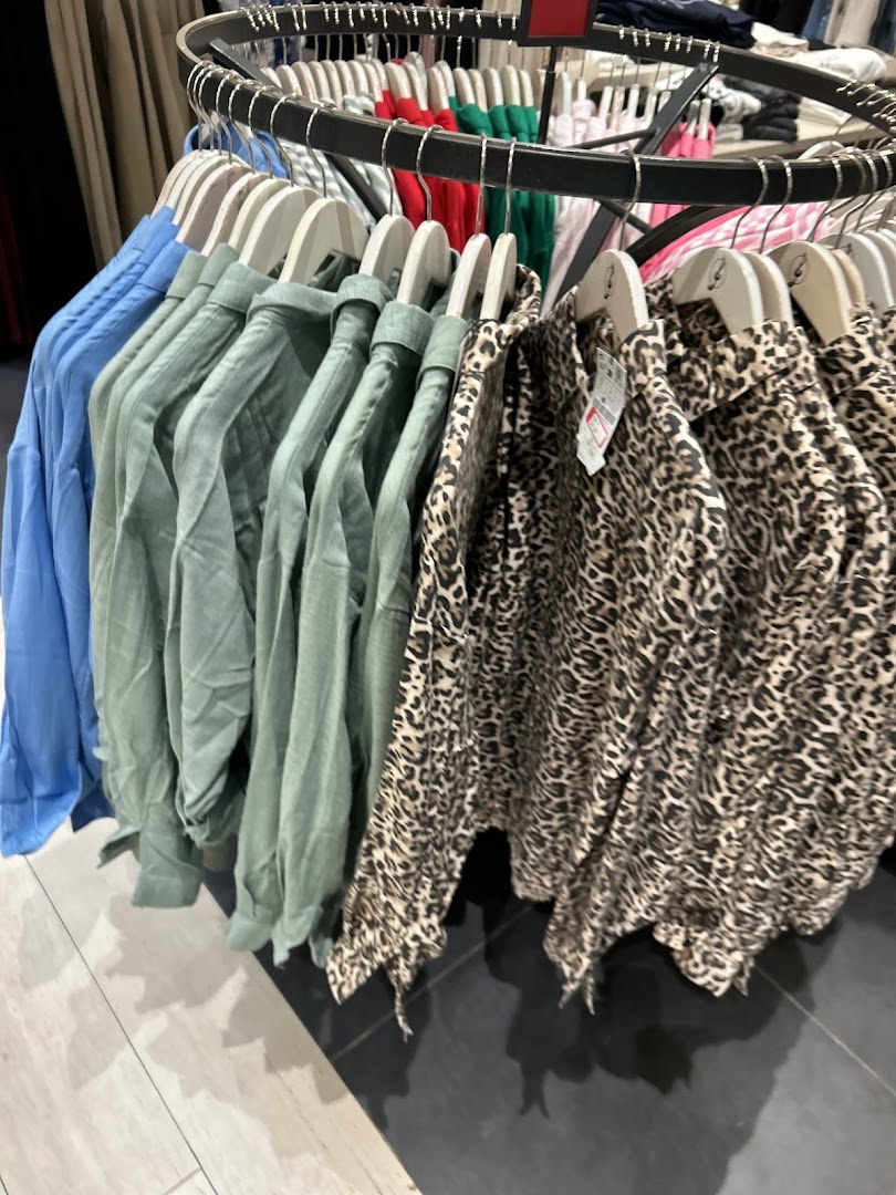 A rack of women's clothing featuring blue, green, and leopard print shirts.