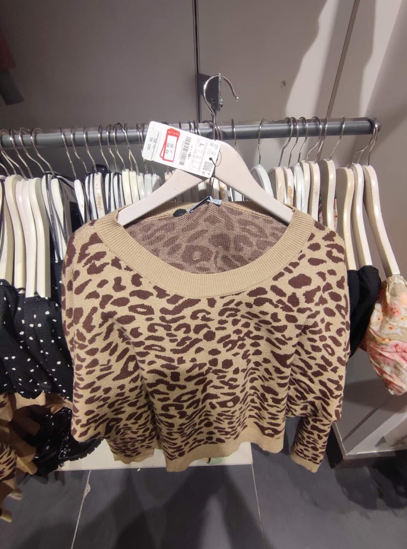A leopard print sweater hanging on a hanger in a clothing store.