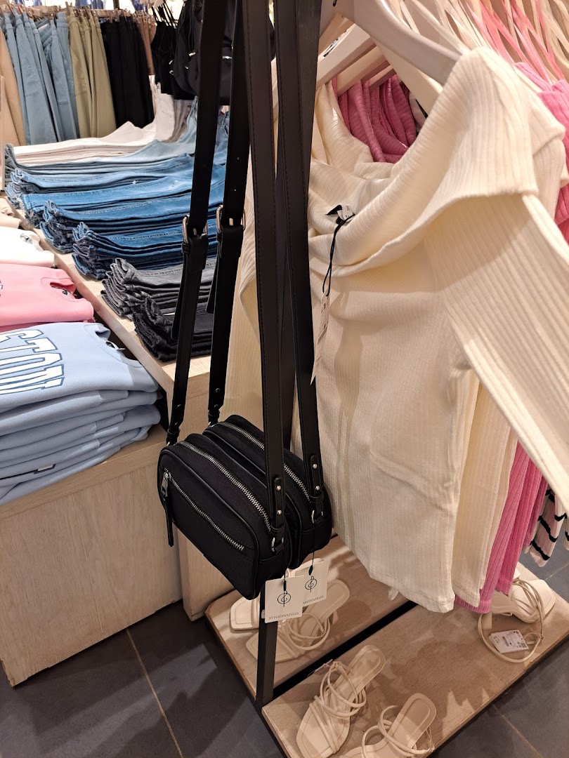 A black crossbody bag hangs in front of folded jeans and stylish tops at Stradivarius.