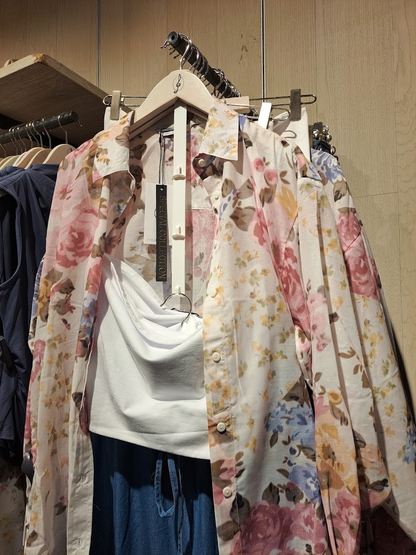 A floral print shirt and white top are displayed on hangers in a clothing store.