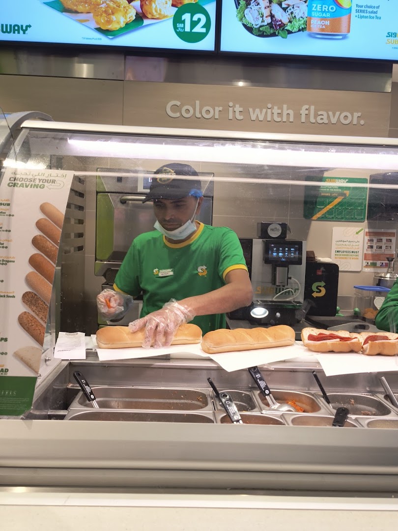 A Subway employee prepares sandwiches behind a counter filled with ingredients.