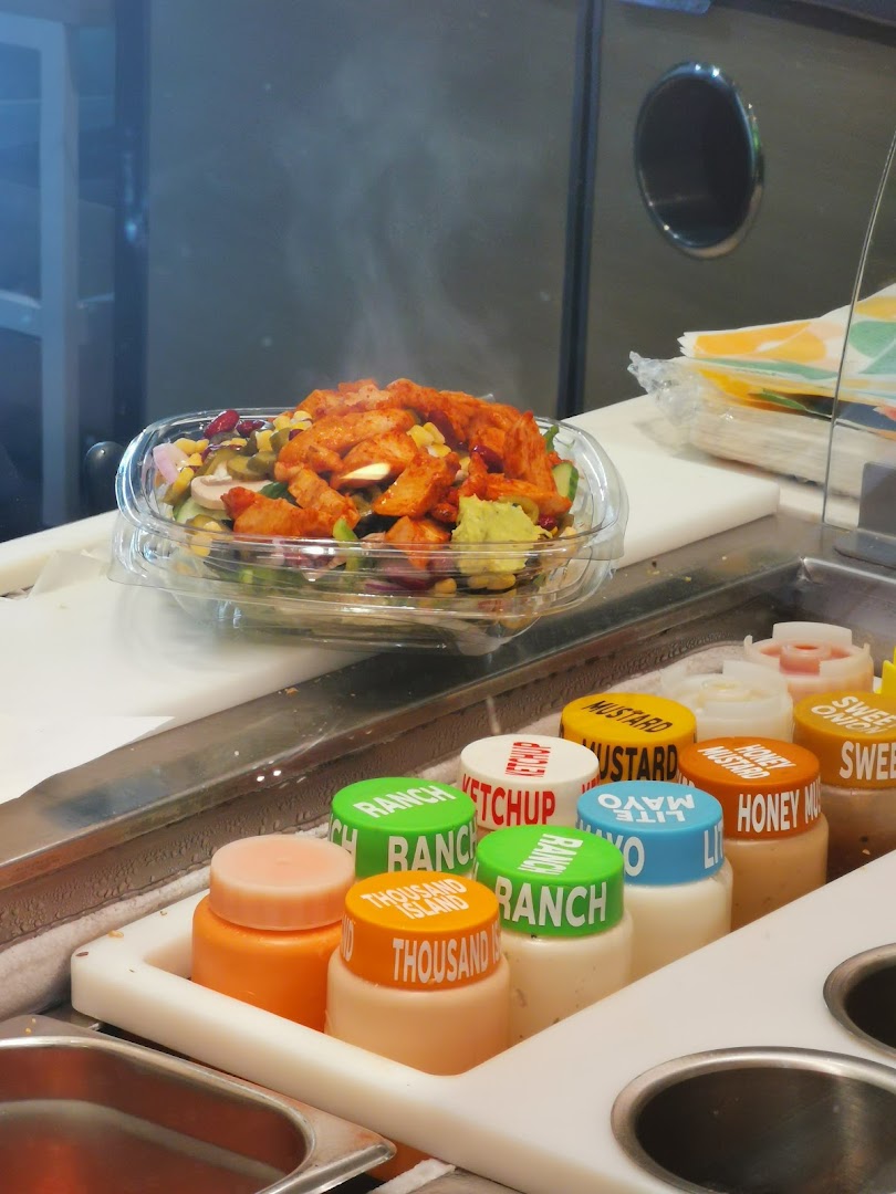 A fresh salad with chicken and various vegetables, with sauce bottles in the foreground.