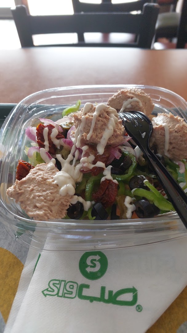 A close-up of a Subway tuna salad with vegetables and dressing in a clear container.