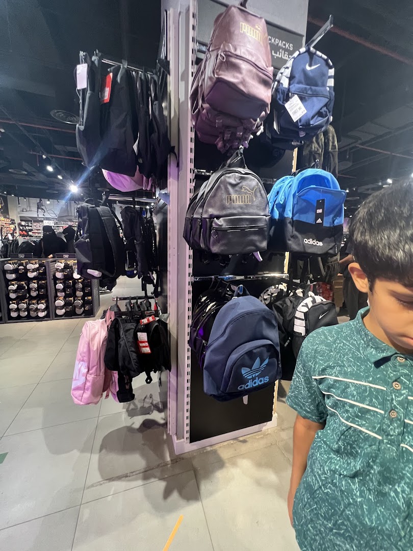 A display of various branded backpacks, including Puma and Adidas, in a retail store.
