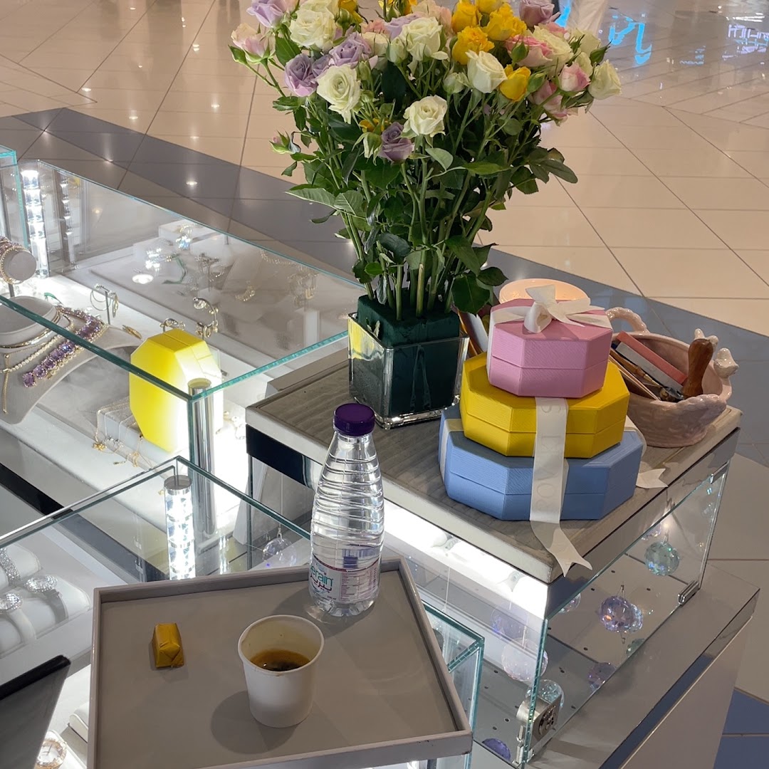 A display of jewelry, gift boxes, flowers, and refreshments in a retail store.
