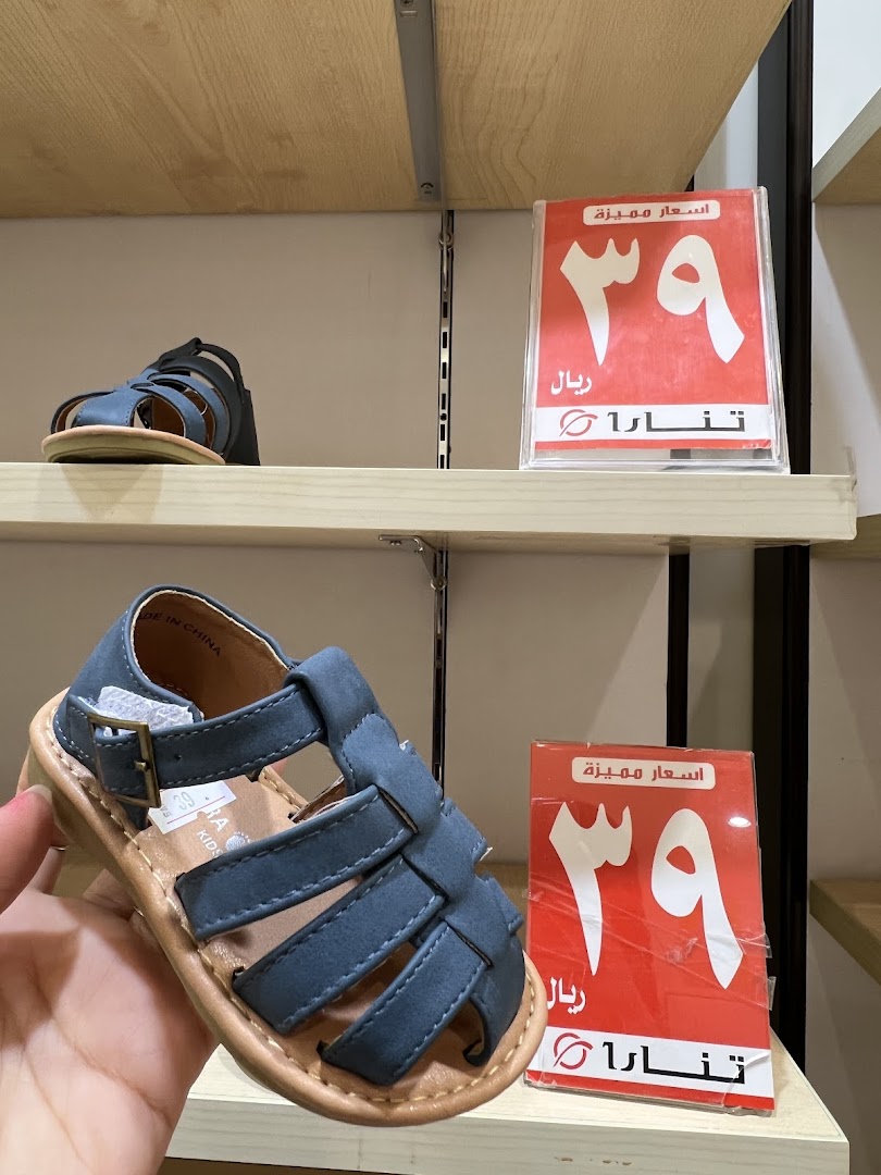 A hand holds a blue sandal with a price tag of 39 riyals.