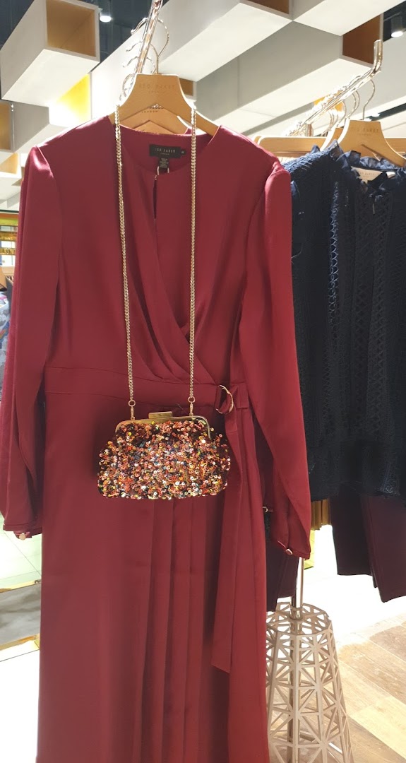 A burgundy dress and a sequined clutch are displayed on hangers in a retail store.
