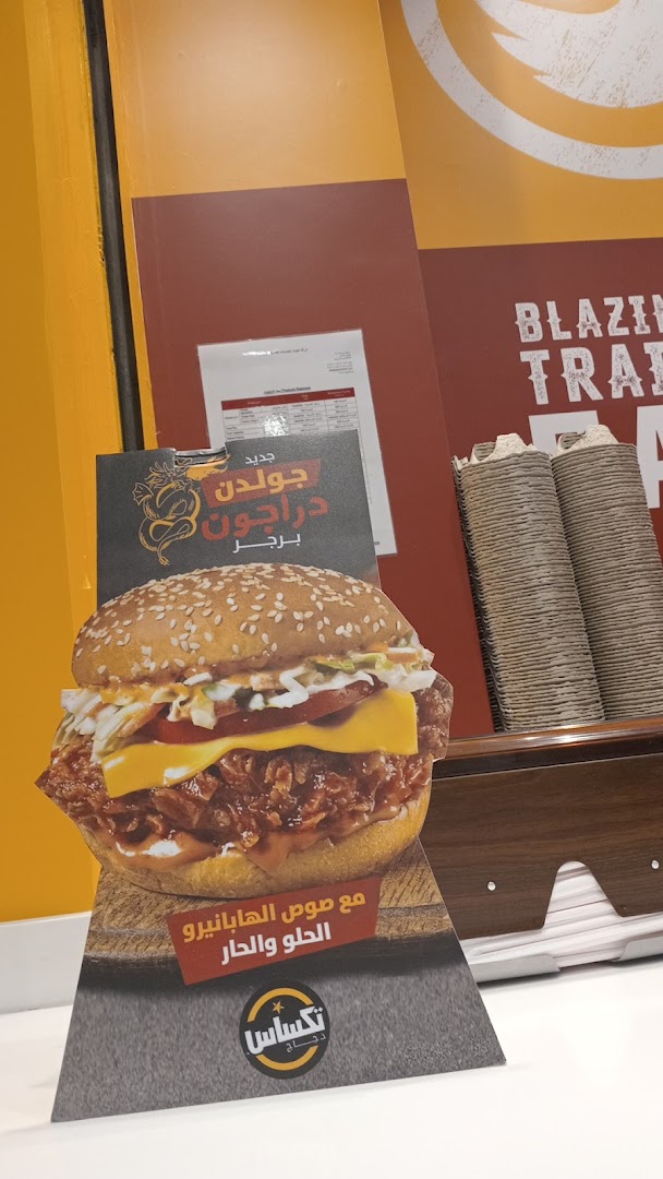 A promotional stand for Texas Chicken featuring a large burger and Arabic text.