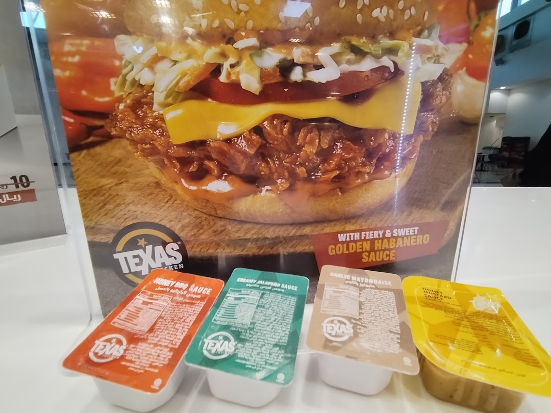 A close-up of a Texas Chicken burger with four sauce cups in front.