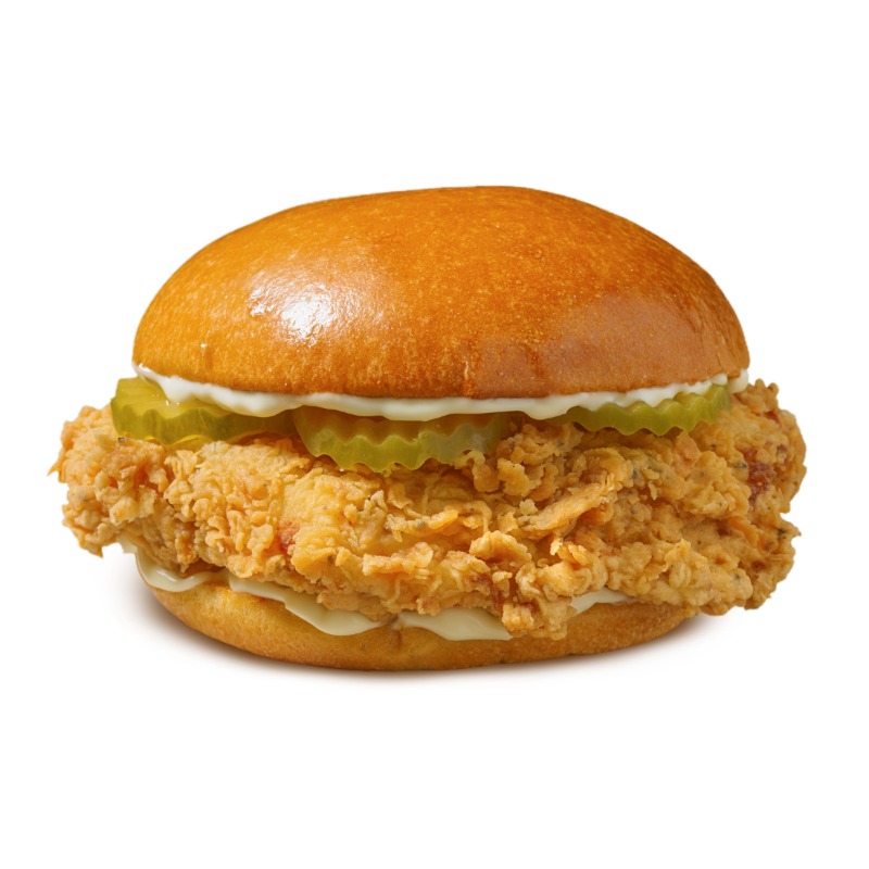 A close-up shot of a crispy fried chicken sandwich with pickles and mayonnaise on a bun.