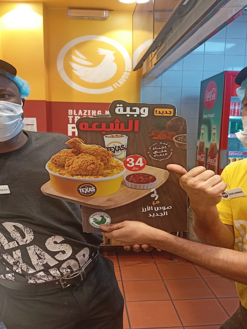 Two men in masks and hairnets hold up a promotional sign for Texas Chicken.