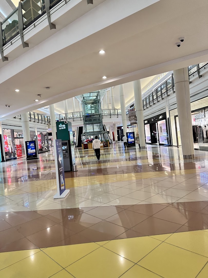 A person walks through a brightly lit shopping mall with multiple stores visible.