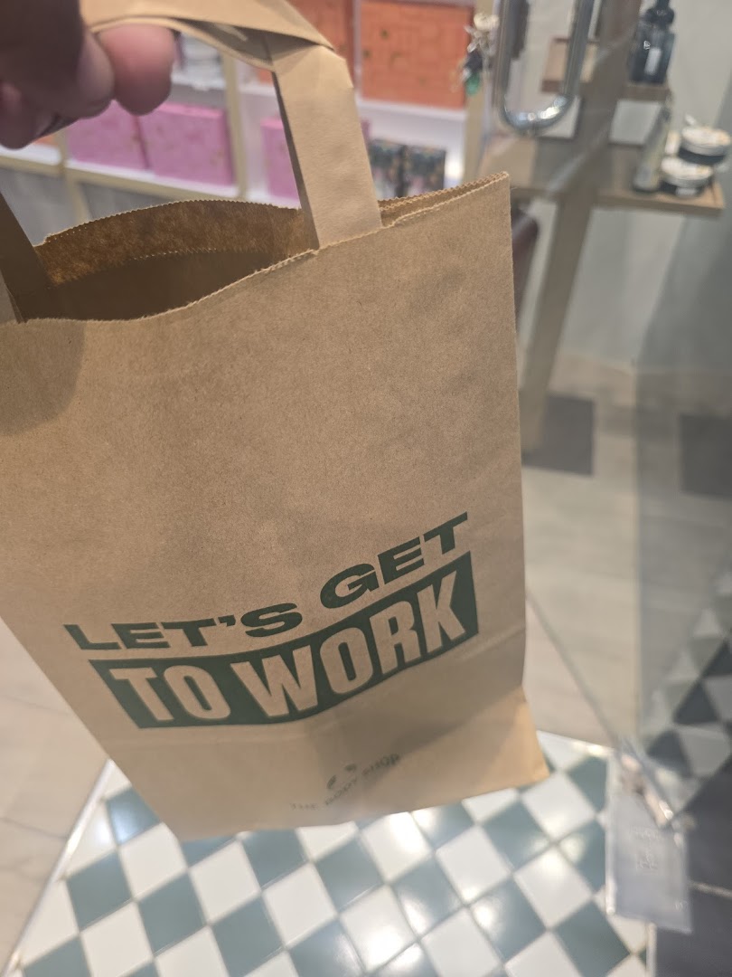 A person holds a brown paper shopping bag from The Body Shop with a motivational slogan.