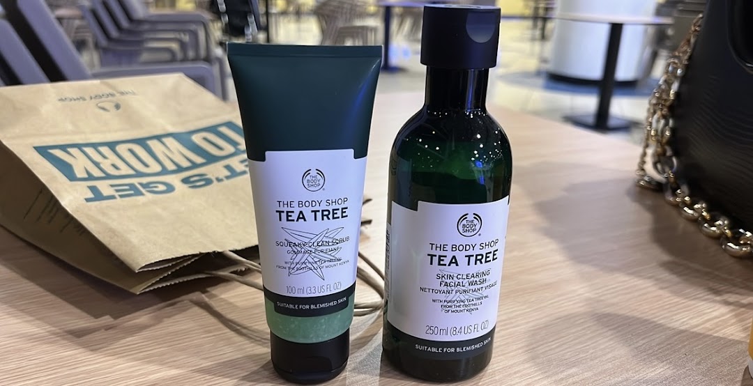 The Body Shop Tea Tree facial scrub and facial wash products are displayed on a wooden surface.