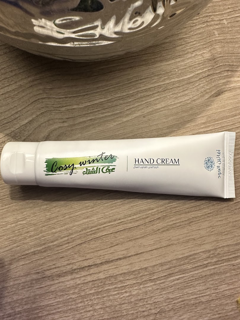 A tube of hand cream with 'Cosy Winter' and Arabic text on a wooden surface.