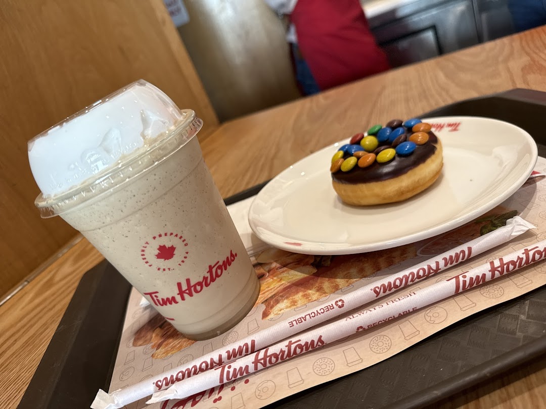 A Tim Hortons milkshake and a chocolate donut with candy toppings on a tray.