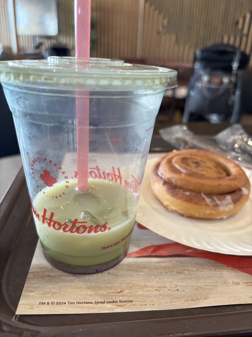 A close-up of a green beverage with a pink straw and a cinnamon bun on a tray.