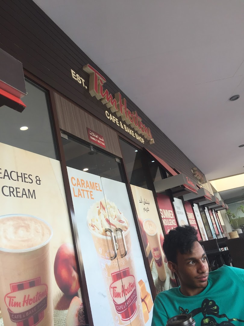 Exterior of a Tim Hortons cafe and bake shop with promotional posters and a customer.
