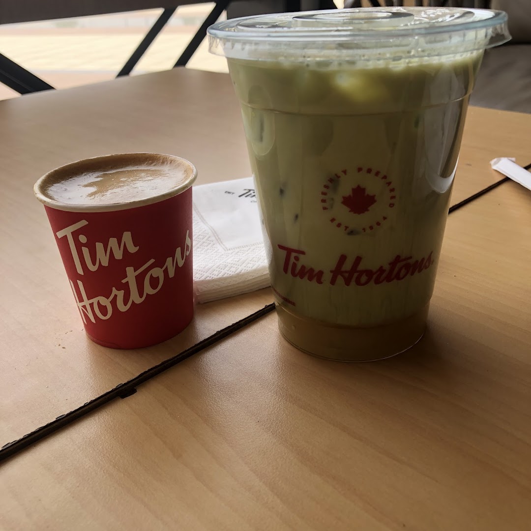 A small red cup of coffee and a large iced beverage from Tim Hortons on a wooden table.