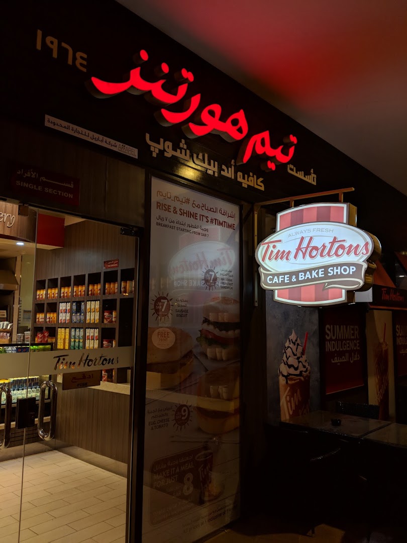 The exterior of a Tim Hortons cafe and bake shop with illuminated signage and a display of food items.