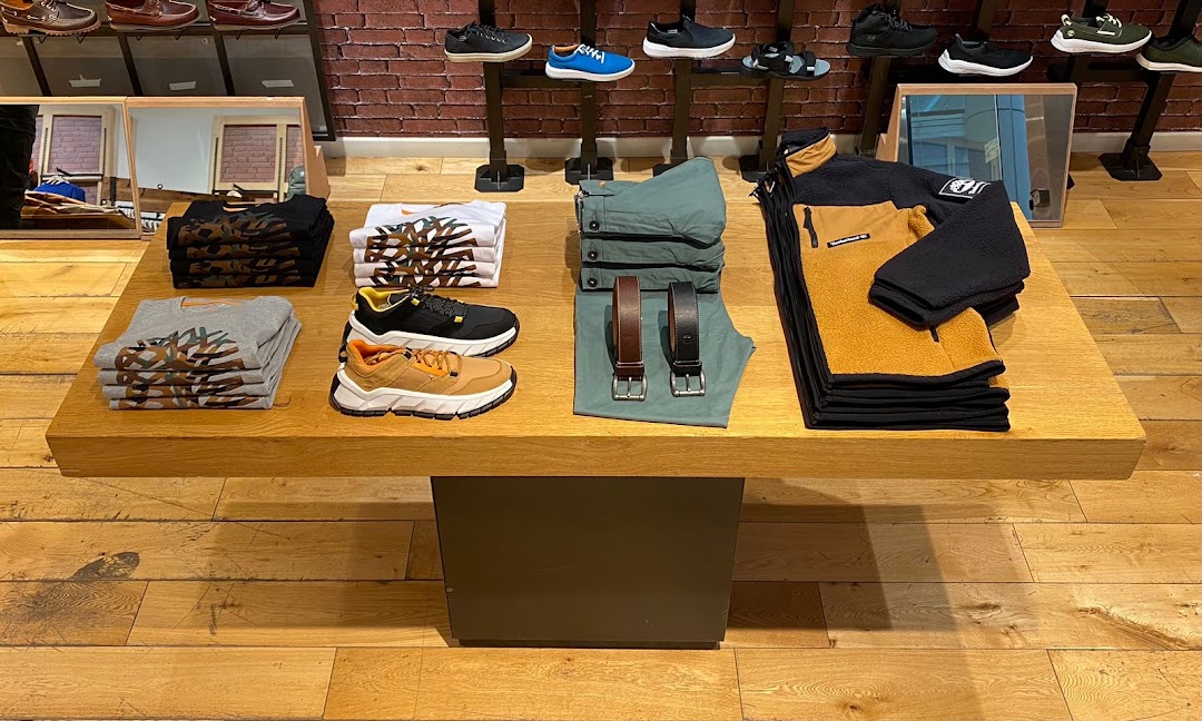 Timberland store display featuring stacked apparel, shoes, and belts on a wooden table.