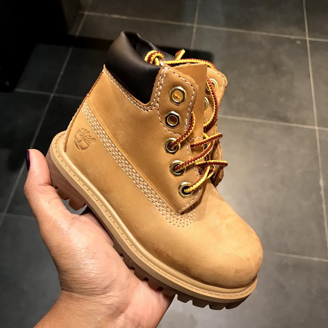 A hand holds a classic tan Timberland boot for children.