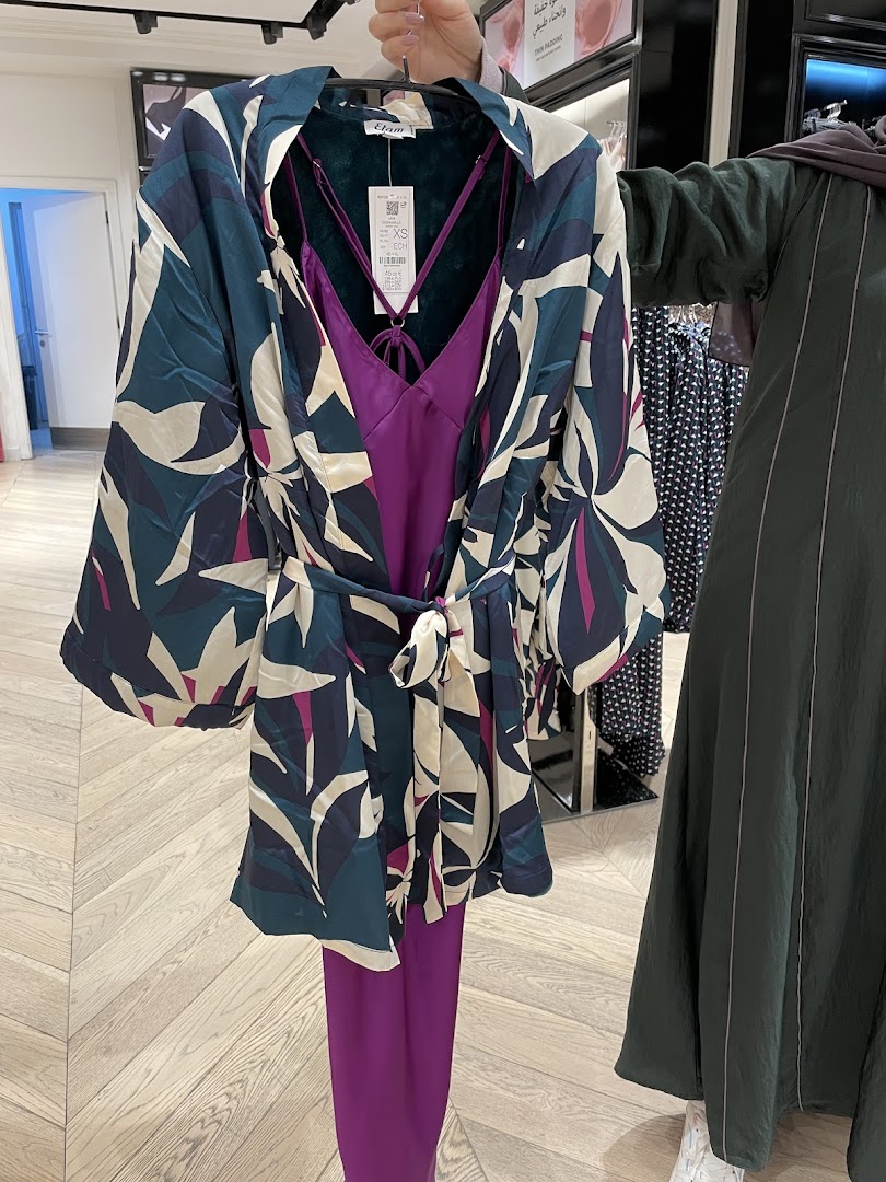 A person holds up a patterned robe over a purple slip dress and pants.