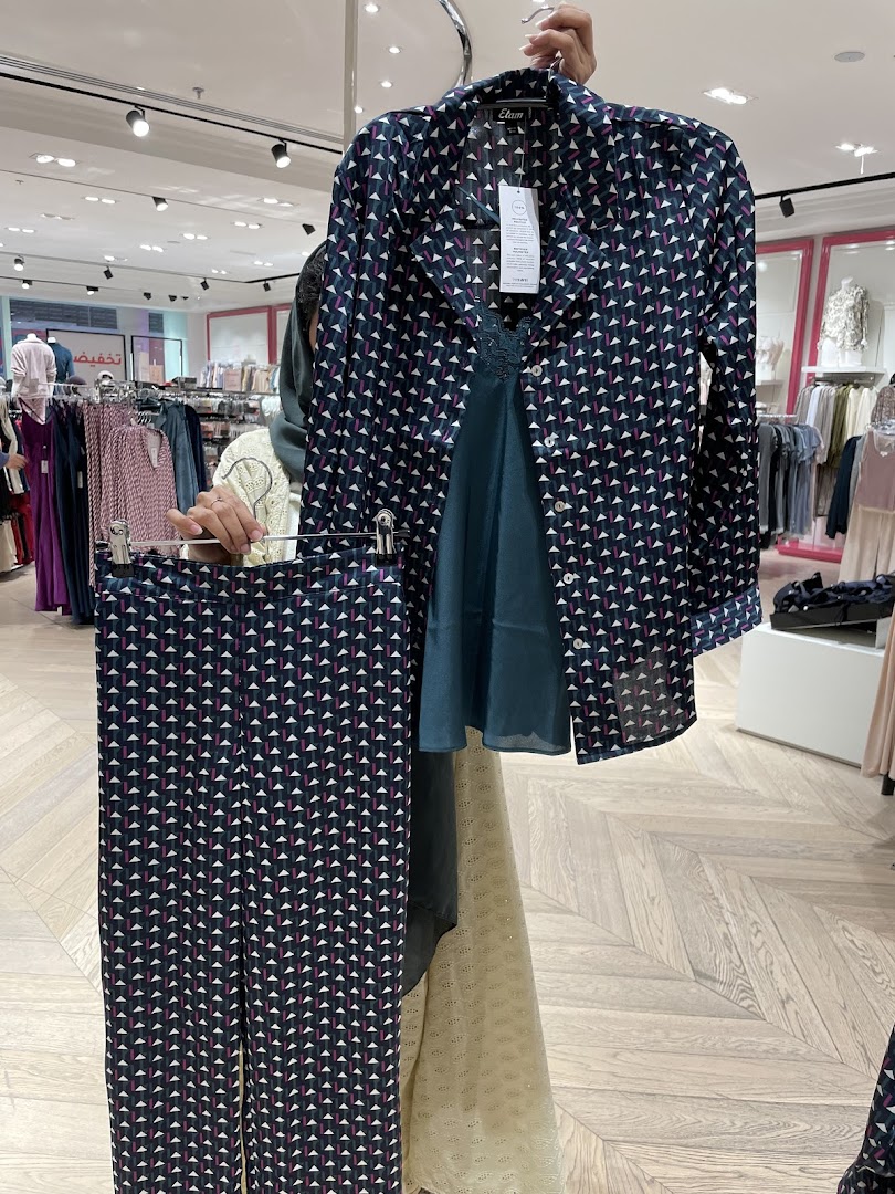 A person holds up a patterned shirt and matching pants from the Etam store.