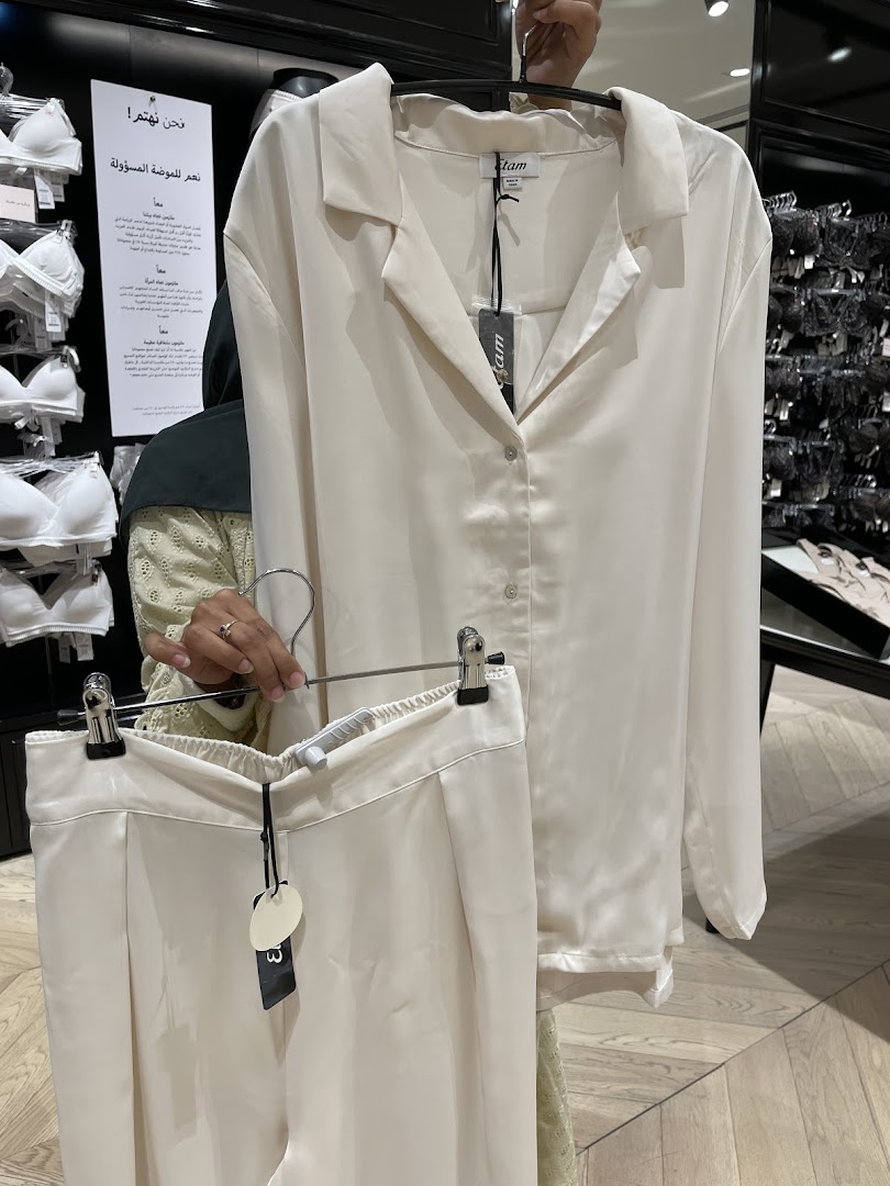 A person holds up a cream-colored satin pajama set in a clothing store.