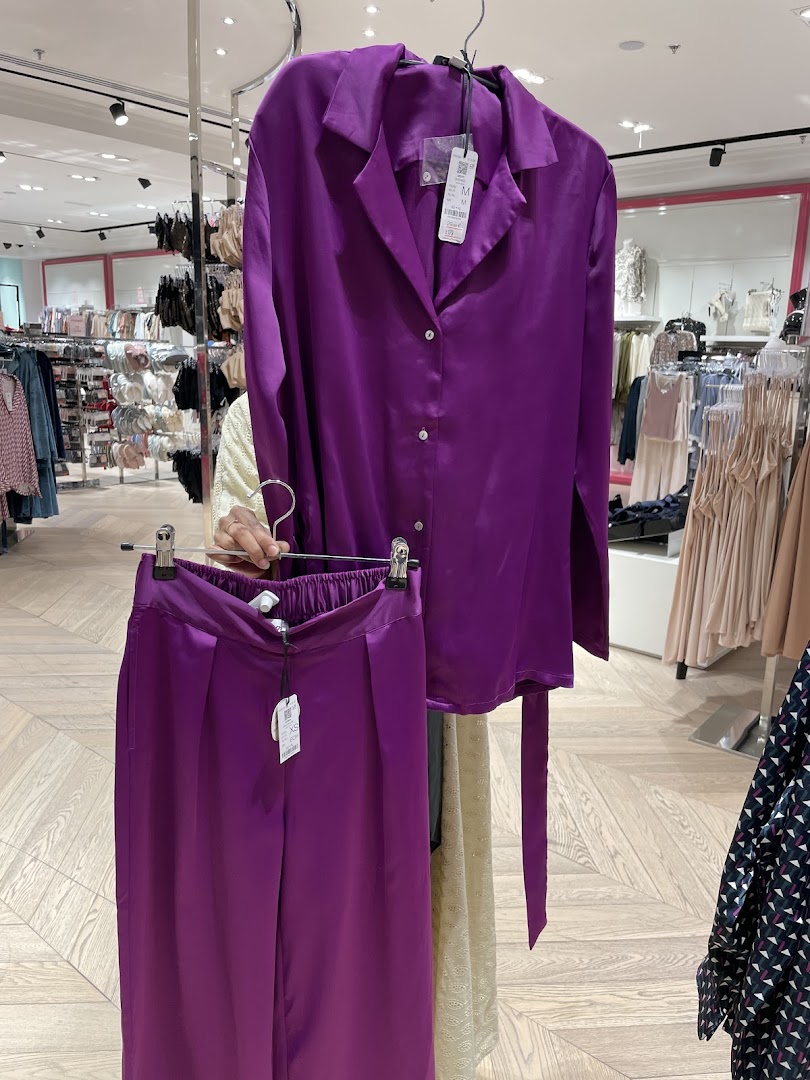A person holds up a purple satin pajama set in a clothing store.