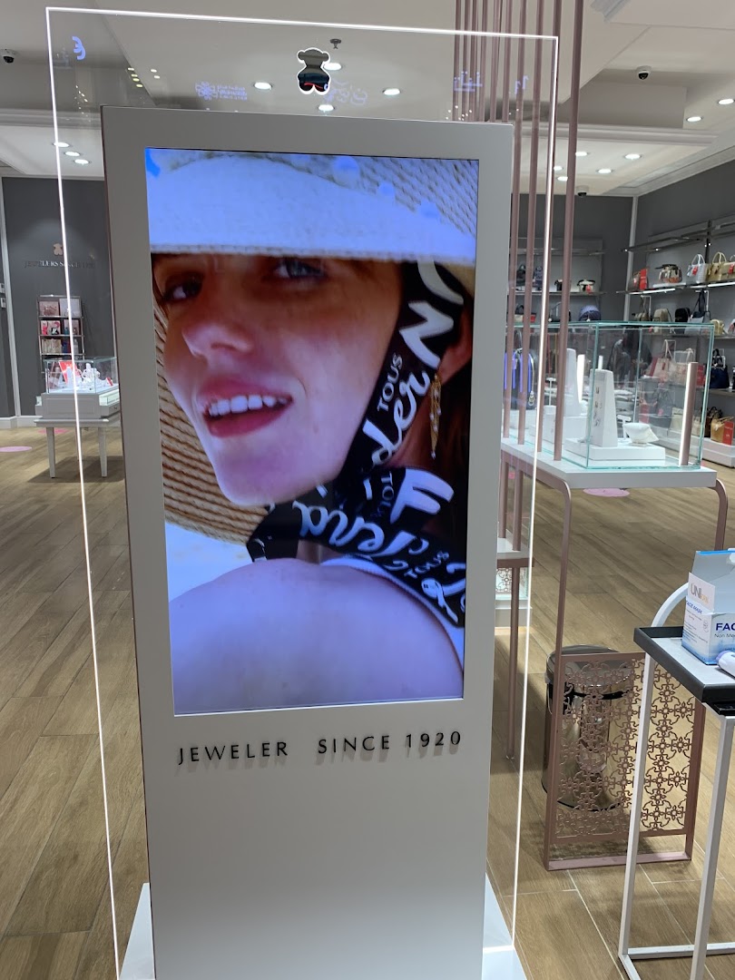 A digital display inside a jewelry store shows a model wearing a hat and jewelry.