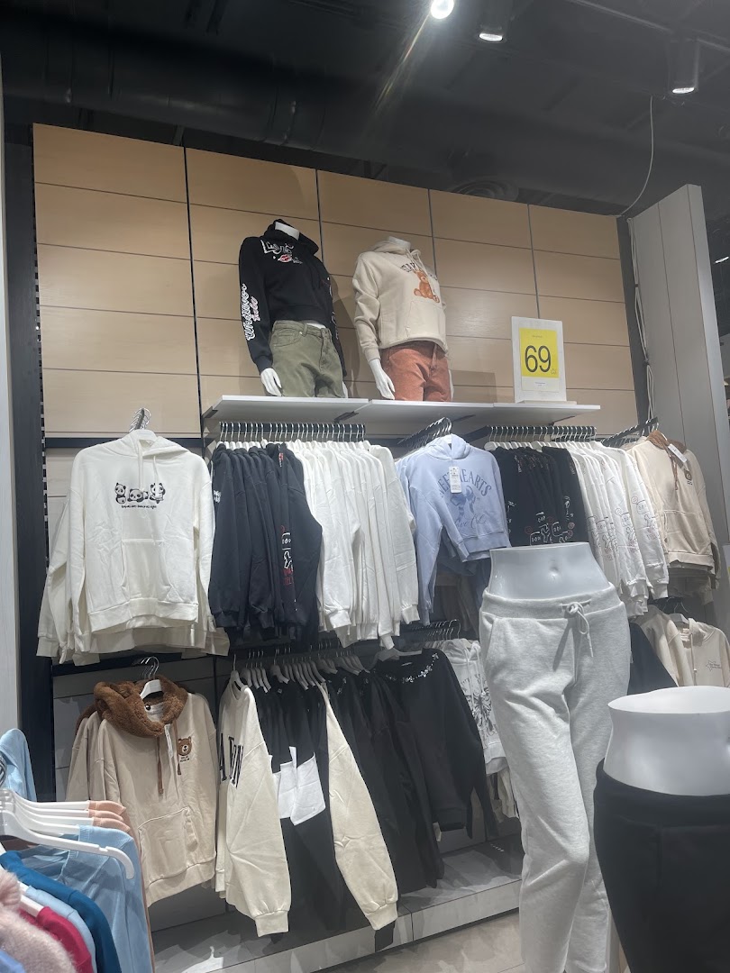 Mannequins display hoodies and sweatpants, with racks of clothing in a retail store.