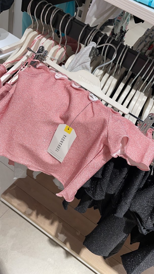 A pink sparkly top with ruffled edges hangs on a hanger in a clothing store.