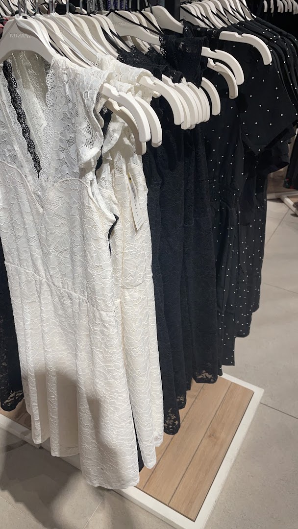 A row of dresses, including white lace and black polka dot styles, hanging on hangers.