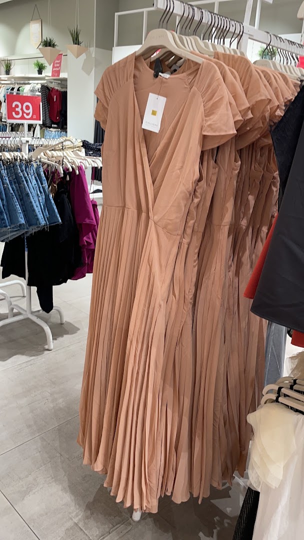 A display of pleated dresses in a clothing store, with a sale sign visible.