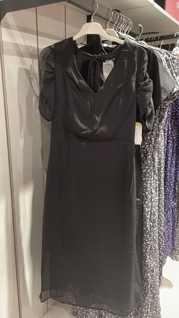 A black dress with a bow detail on the back is displayed on a hanger.