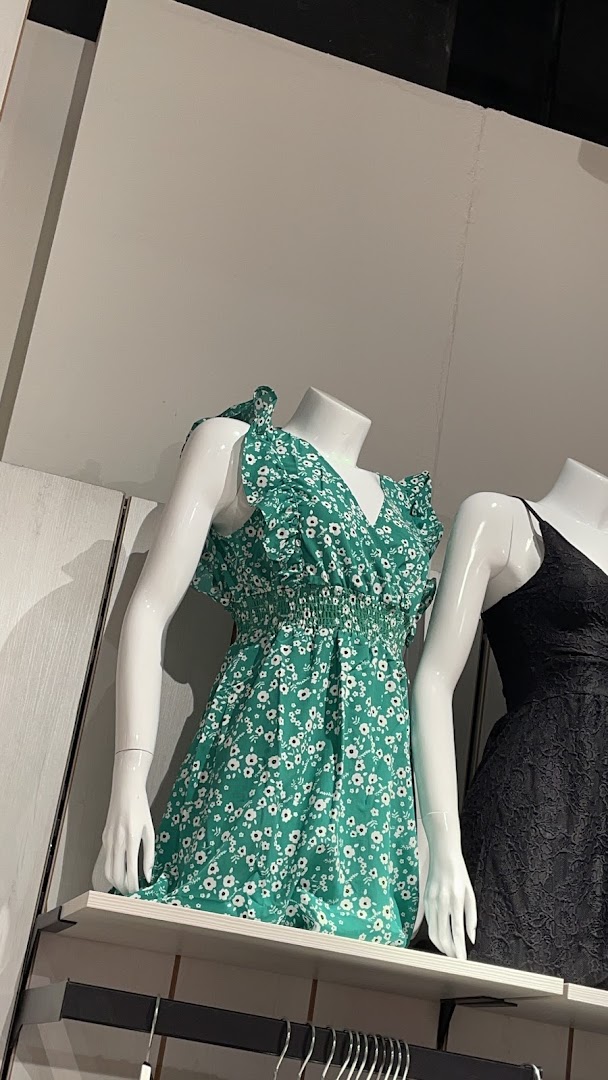 Mannequins display a green floral dress and a black lace dress in a retail store.