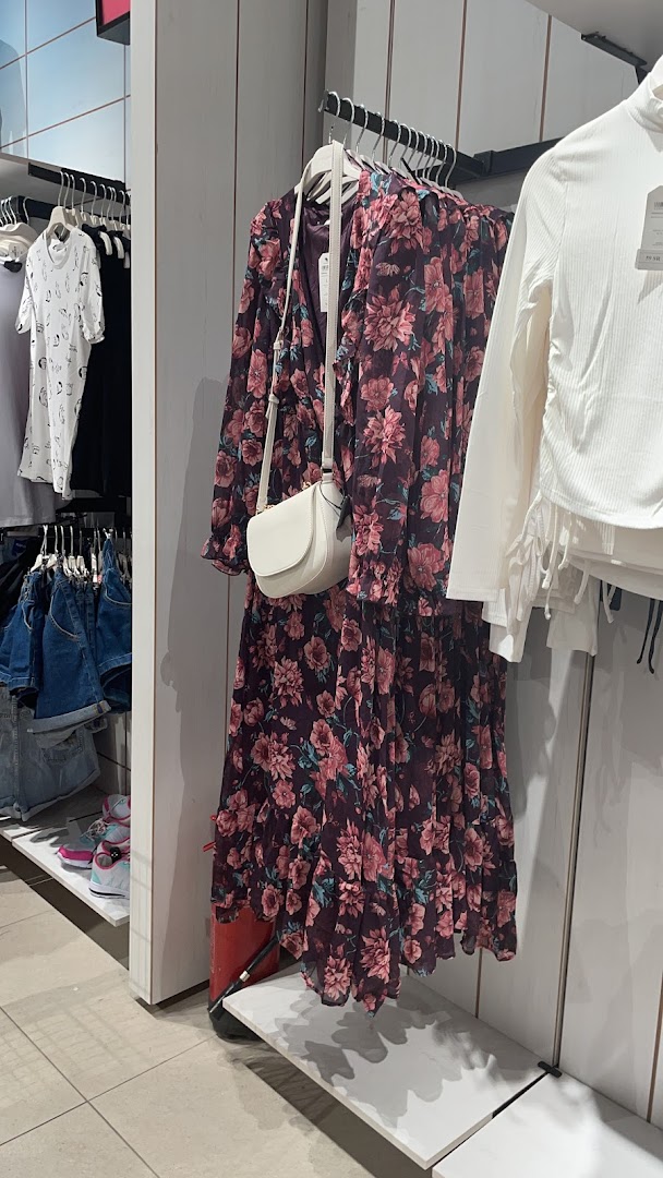 A floral dress and white top are displayed on hangers in a clothing store.