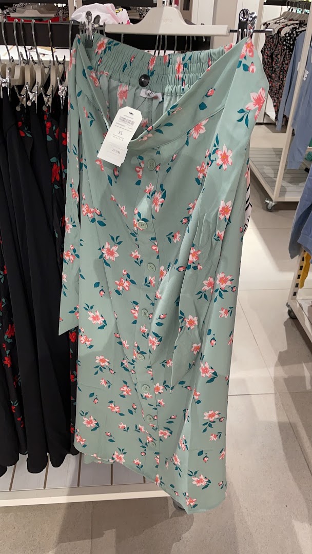 A light green floral print skirt with buttons down the front is displayed on a hanger.
