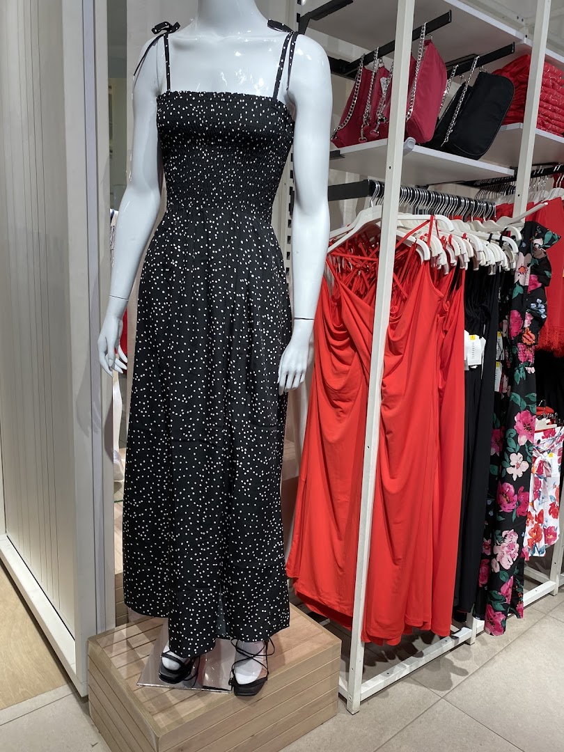 A mannequin displays a black polka dot dress next to racks of colorful clothing and handbags.
