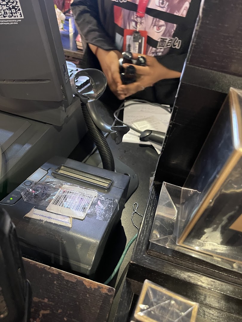 A close-up of a retail counter with a scanner, receipt printer, and a person holding items.